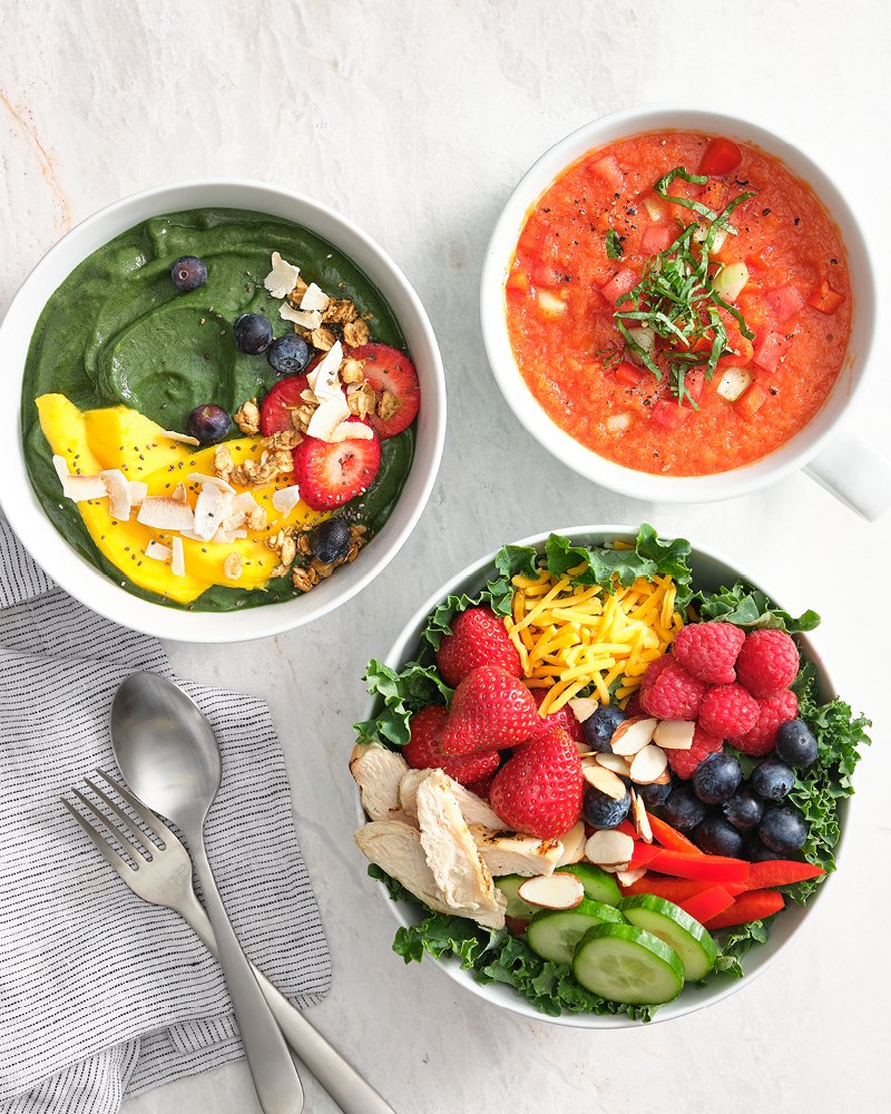 Three colorful bowls of fresh produce and soup