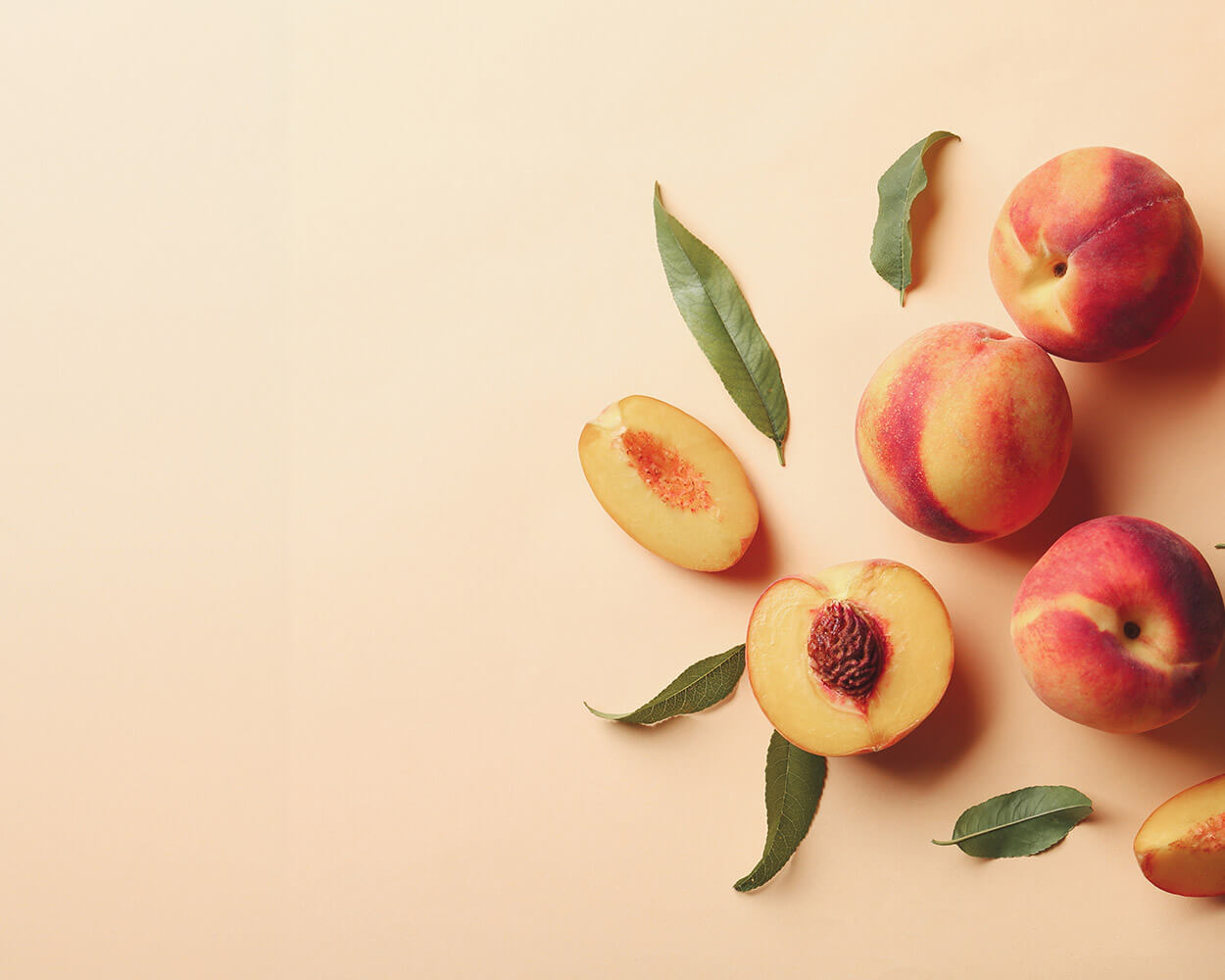 Sliced and Whole Peaches on Peach colored background with leaves